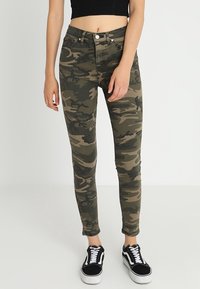 Kamouflage skinny jeans i gröna och bruna nyanser, med fem fickor, dragkedja med knappstängning och en åtsittande passform. Kombineras med svarta sneakers.