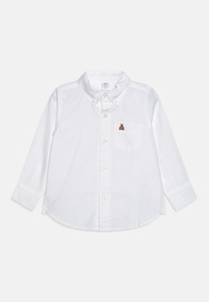 White long-sleeve shirt made of cotton, featuring a button-down collar, front pocket, and a small brown bear embroidery.