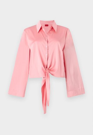 Rosa sateng cropped skjorte med lange ermer, knappestolpe foran og knytedetalj i midjen. Har en klassisk krage for et strukturert utseende.