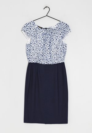 Biała i granatowa sukienka z krótkimi rękawami, z granatowymi kropkami na białej górze i jednolitym granatowym ołówkowym spodem, wisząca na czarnym wieszaku.