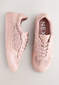 Baskets roses dotées de dentelle florale texturée, accents en cuir lisse et une semelle en caoutchouc souple. Design à lacets avec détails brodés.