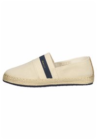 Beige canvas espadriller med ett marinblått elastiskt band och en flätad jutesula. Har en etikett på ovansidan och en svart sula.
