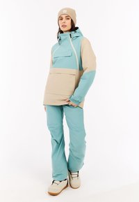 Leichte, zweifarbige Jacke in Türkis und Beige mit verstellbarem Kapuzen, Fronttasche und passenden türkisen Hosen; weist strukturierte Akzente auf.