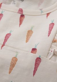 Ljust beige tyg med ett upprepat mönster av färgglada morötter i röd, orange och grön, med en texturerad yta och samlad detalj.