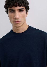 Suéter de punto azul marino con cuello redondo. Presenta una textura suave y una silueta ajustada, exhibido en una modelo con cabello corto y rizado.