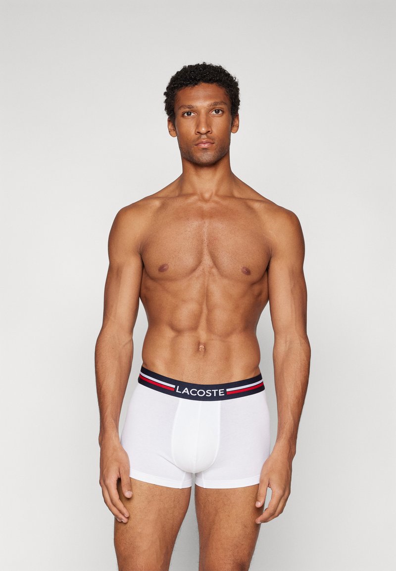 Weiße Baumwollboxershorts mit einem marineblauen Bund, der rot-weiße Streifen aufweist, und dem Markennamen prominent an der Vorderseite.