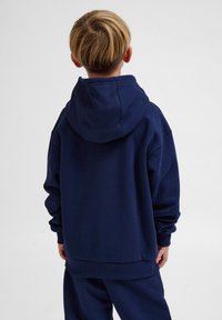 Mörkblå hoodie i mjukt material, med en stor huva, avslappnad passform, ribbade ärmslut och nederkant, designad för komfort och avslappnat bruk.