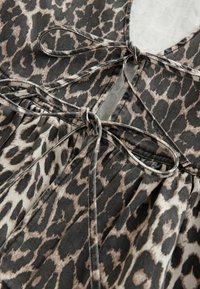 Leopardenmusterstoff mit schwarzen und beigen Flecken. Hat Bindebänder am Ausschnitt und gefältelte Details mit einer sanften Textur.