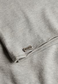 Tissu gris clair plié avec une petite étiquette métallique rectangulaire cousue près du bord, gravée de "SDRY".