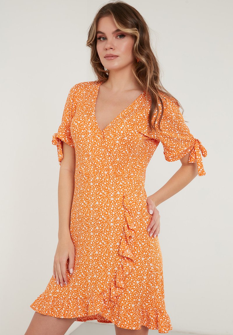 Oranje bloemenjurk met een v-hals, korte pofmouwen en ruches. Gemaakt van lichte stof met een getailleerde taille en een uitlopende rok.