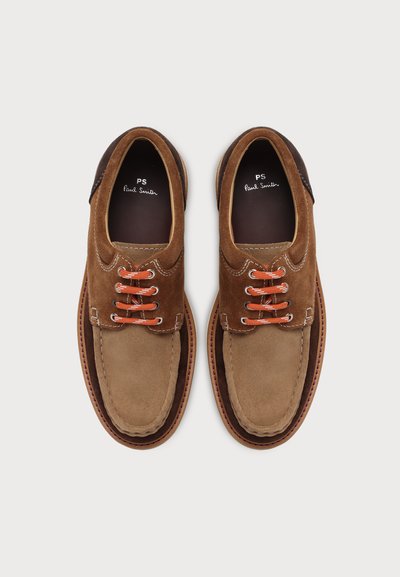 Paire de chaussures décontractées en suède marron à lacets orange et détail de couture sur fond neutre.