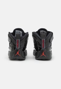 Ett par svarta Air Jordan-sneakers sedd bakifrån med röd Jumpman-logotyp och Jordan-text på hälla.