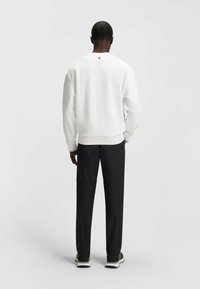 Felpa bianca con colletto rotondo, polsini e orlo a coste. Accoppiata con pantaloni neri con dettagli di cucitura e design aderente.