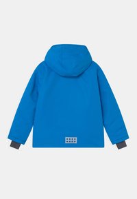 Huvtröja i klarblått, med långa ärmar och en rektangulär logotapp med cirklar på baksidan. Slät, vattentålig material.