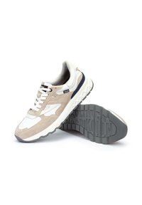 Zapatillas beige y blancas con materiales de ante y malla, forma redondeada, diseño con cordones y suela de goma texturizada con patrones geométricos.