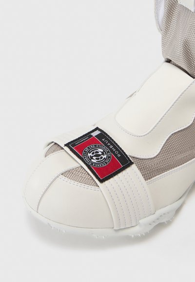 Baskets blanches de sport avec une tige en mesh texturée, un bout renforcé, une sangle proéminente avec logo et une semelle à picots pour une meilleure traction.