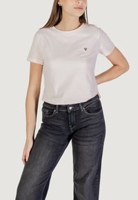 T-shirt a maniche corte rosa chiaro in cotone, con un piccolo logo a triangolo sul lato sinistro del petto, abbinato a jeans grigi scuri.