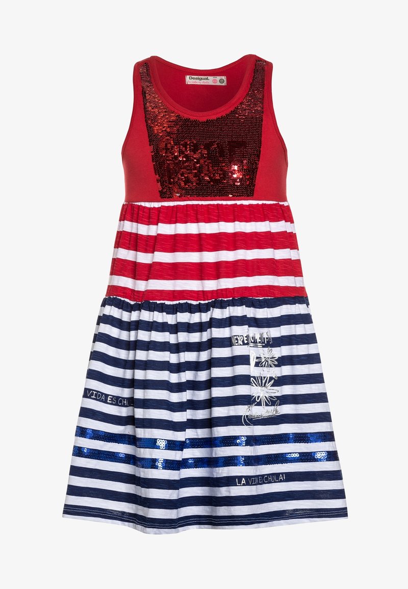 Punast tank-kleiti, millel on säraaktsentiga pluus, mis sisaldab horisontaalseid punaseid ja valgeid ridasid ülaserval ning tumesiniseid ja valgeid ridasid seeliku osas.