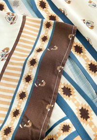 Tissu avec des rayures marron, beige et bleues et des motifs floraux. Surface texturée, présentant des designs de lignes contrastées et des détails ornés.