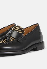 Black leather loafers with a tassel accent, featuring a zebra-patterned fabric panel on the vamp and a smooth finish. Classic design and shape.
