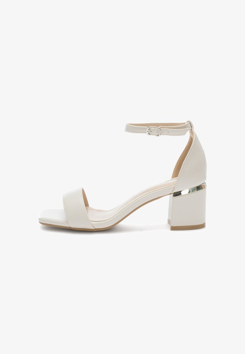 Białe sandały na obcasie z szerokim paskiem na palce i paskiem wokół kostki, z błyszczącym srebrnym akcentem na słupku. Gładka, przypominająca skórę tekstura.