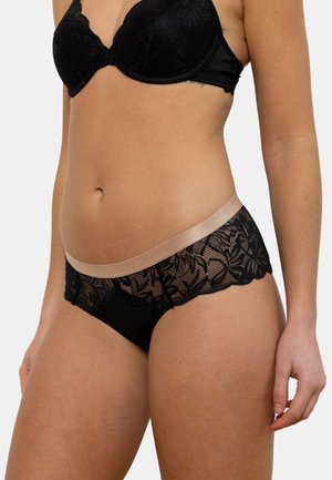 Sous-vêtements en dentelle noire avec un motif floral et une taille couleur beige. Présente des panneaux transparents sur les côtés et un design à bord festonné.
