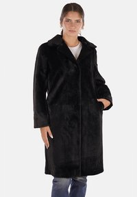 Cappotto in pelliccia sintetica nera con colletto a scollo a V, maniche lunghe e tasche laterali; texture liscia con una silhouette dritta e slanciata.