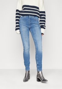 Vaqueros skinny de denim en un azul claro con un efecto deslavado. Presentan un estilo clásico de cinco bolsillos y una cintura de media altura. Combinados con botines metálicos de tobillo.
