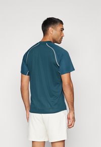 Aqua-kleurige sportshirt met korte mouwen, gemaakt van een lichte, ademende stof; heeft grijze accenten langs de schouders en de rug.