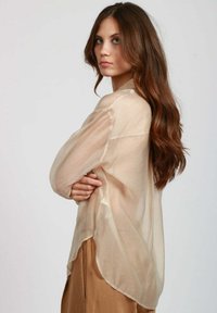 Camicia beige trasparente con maniche lunghe, chiusura con bottoni frontale e orlo curvo. Tessuto leggero e texture leggermente traslucida.