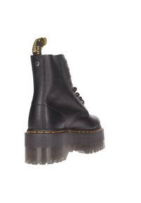 Bottine en cuir noir avec une semelle en caoutchouc transparent épaisse, des coutures jaunes et une languette à l'arrière. Dispose de six œillets pour les lacets.