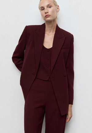 Bordeaux op maat gemaakte blazer met scherpe revers, gecombineerd met een bijpassend mouwloos topje met drie knopen en slim-fit broeken.
