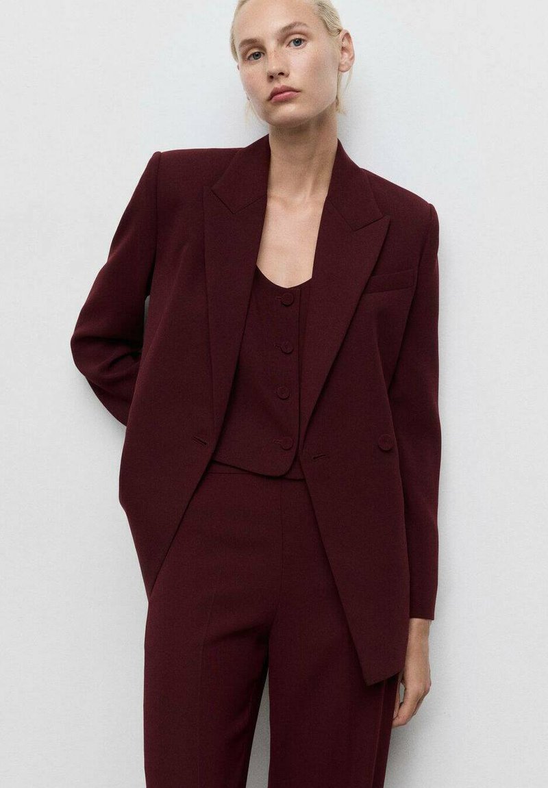 Burgundin räätälöity bleiseri terävillä läpillä, yhdistettynä samasta kankaasta valmistettuun hihattomaan toppiin, jossa on kolme nappia, sekä slim fit -housuihin.