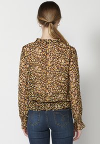 Blusa trasparente con motivo floreale arancione e giallo su sfondo nero. Caratterizzata da maniche lunghe e orlo arricciato.