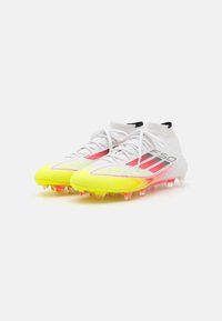 Bottes de soccer blanches avec des accents jaunes vifs et roses, un upper texturé, un design élégant et des crampons transparents sur la semelle.