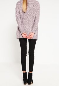 Långärmad, ljuslila stickad tröja med ett strukturerat mönster, i kombination med smala svarta byxor och svarta klackiga ankelskor.