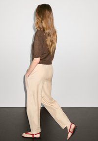 Hnědý pletený top, béžové široké kalhoty a červené sandály na svůdné šňůrce. Tento outfit má uvolněný střih a jednoduchý design s kontrastními barvami.