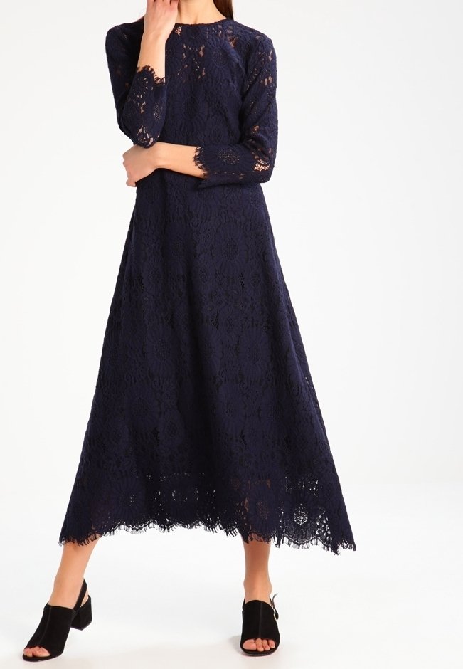 Granatowa sukienka z koronką, z długimi rękawami i rozszerzanym krojem; posiada misternie wykonane kwiatowe wzory oraz falbankę u dołu. Czarne buty na słupku.