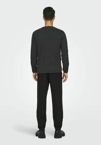 Grijze langemouwen shirt met een ronde hals, gecombineerd met zwarte broek. Het shirt heeft een gladde textuur en ribbelmanchetten; de schoenen hebben een dikke zool.