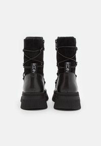 Zwarte enkelboots met een combinatie van suede en leren materialen, veters, een opvallende ribbelzool en logo-opdruk aan de achterkant.