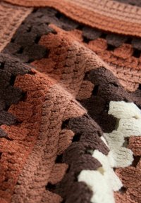 Kvačkani pokrivač s teksturiranim, patchwork dizajnom koji predstavlja nijanse smeđe, bež i kreme u geometrijskom uzorku.