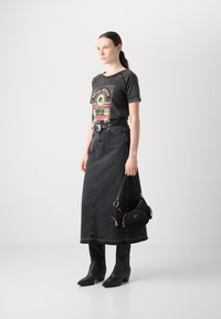 Maglietta nera grafica a maniche corte, abbinata a una gonna maxi in denim scuro e stivali cowboy in pelle nera. Borsa nera con dettagli in zip.
