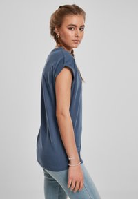 Sininen puuvillainen t-paita rentolla istuvuudella, käännetyt hihat ja pyöreä kaula-aukko. Yhdistetty vaaleansinisiin farkkuihin, jotka näyttävät sileältä.