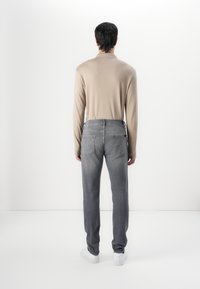 Beige long-sleeve shirt paired with gray denim jeans. The jeans feature two back pockets with decorative stitching, and white sneakers.