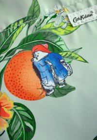 Tessuto a fantasia floreale con un arancione, foglie e un orso in giacca blu con un cappello rosso. L'etichetta recita "Cath Kidston."