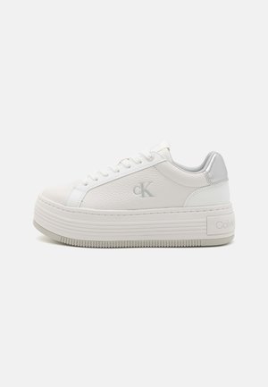 Biały sneaker na platformie z sznurowadłami, teksturowaną skórą, szarym logo "cK" po boku oraz oznaczeniem "Calvin Klein" na grubej podeszwie przy pięcie.