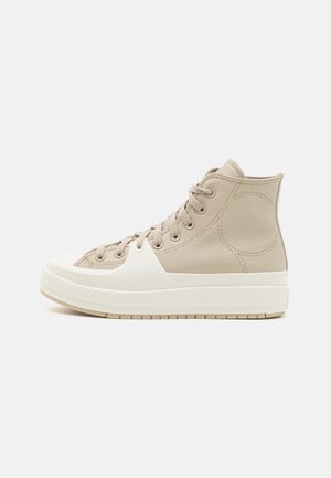Baskets montantes en cuir beige clair avec un embout et une semelle en caoutchouc blanc, dotées d'un système de laçage et d'accents texturés.