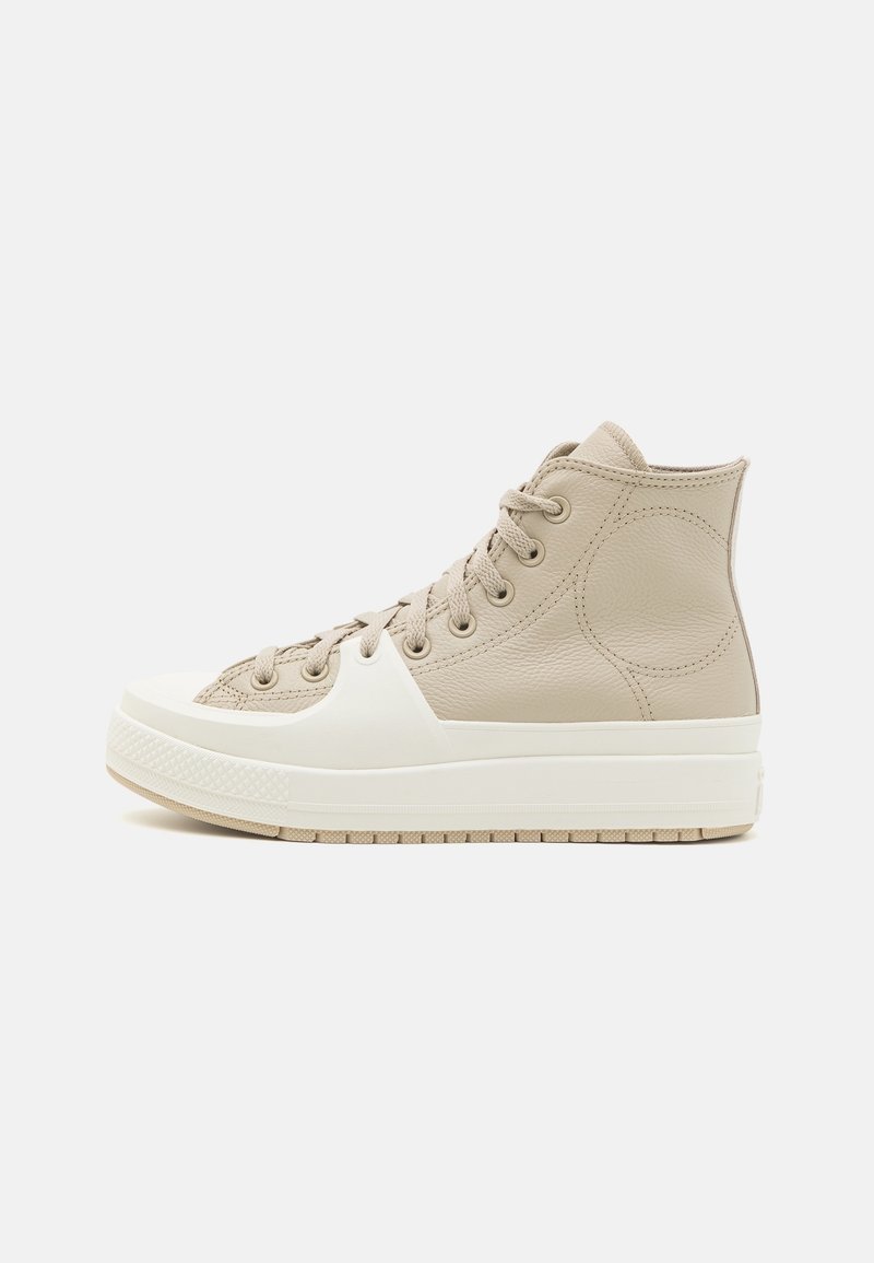 Baskets montantes en cuir beige clair avec un embout et une semelle en caoutchouc blanc, dotées d'un système de laçage et d'accents texturés.