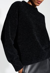 Schwarzer, strukturierter Strickpullover mit hohem Kragen und oversized Passform. Mit gerippten Bündchen und Saum, kombinierbar mit einer Lederhose.