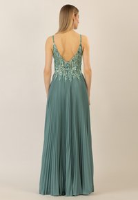 Abito da sera teal con profondo scollo a V sul retro, corpetto decorato con paillettes e gonna plissettata. Le spalline sono sottili e regolabili.